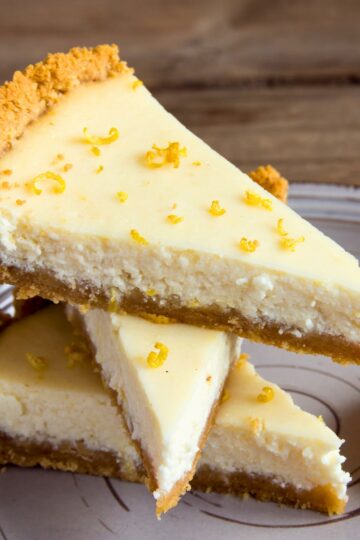 Slices of light lemon pie stacked on a plate with creamy lemon filling, graham cracker crust, and fresh lemon zest sprinkled on top.