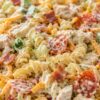 Creamy chicken bacon ranch pasta salad with rotini, grilled chicken, crispy bacon, cheddar, cucumber, cherry tomatoes, and ranch dressing in a white bowl.