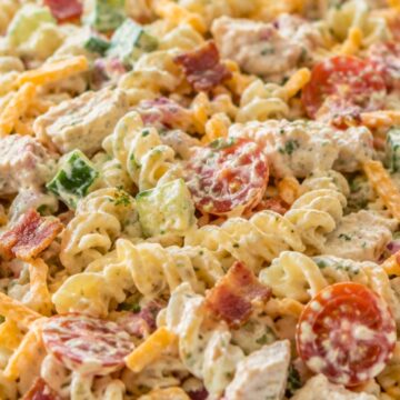 Creamy chicken bacon ranch pasta salad with rotini, grilled chicken, crispy bacon, cheddar, cucumber, cherry tomatoes, and ranch dressing in a white bowl.