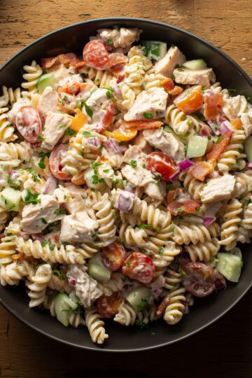 Chicken bacon ranch pasta salad with rotini, diced chicken, crispy bacon, cherry tomatoes, cucumbers, red onion, and creamy ranch dressing.