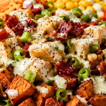 Chicken bacon ranch sweet potato bowl with roasted sweet potatoes, seasoned chicken, crispy bacon, corn, cheddar, green onions, lettuce, and creamy ranch dressing in a white bowl.