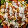 Chicken bacon ranch sweet potato bowl with roasted sweet potatoes, diced chicken, crispy bacon, corn, cherry tomatoes, lettuce, and creamy ranch dressing.