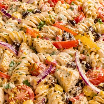 Creamy chicken fajita pasta salad with rotini, chicken breast, black beans, corn, cherry tomatoes, bell peppers, red onion, cilantro, and creamy dressing in a beige bowl.