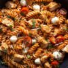 Chicken Parmesan pasta salad with rotini, diced chicken, cherry tomatoes, mozzarella pearls, shredded Parmesan, fresh basil, and tomato sauce.