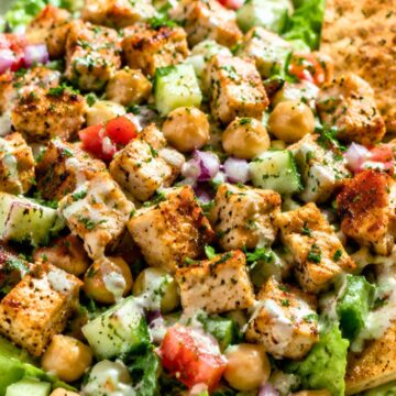 Chicken shawarma chopped salad with grilled chicken, chickpeas, cucumbers, tomatoes, red onion, romaine lettuce, creamy dressing, fresh herbs, and toasted pita chips in a beige bowl.