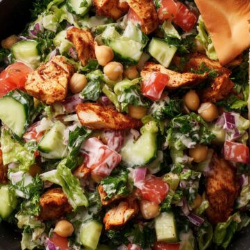 Chicken shawarma chopped salad with seasoned chicken, cucumbers, tomatoes, chickpeas, red onion, lettuce, creamy dressing, and a pita chip.