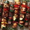 Grilled chicken and steak kabobs with zucchini, red and yellow bell peppers, onions, and fresh rosemary on a parchment-lined tray.