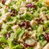 Chopped chicken salad with grapes, pecans, romaine lettuce, celery, green onions, and creamy dressing served in a white bowl with a cracker tucked in the back.