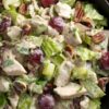 Close-up of creamy chicken salad with chopped chicken, red grapes, pecans, celery, and lettuce.
