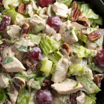 Close-up of creamy chicken salad with chopped chicken, red grapes, pecans, celery, and lettuce.