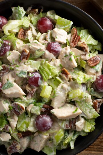 Close-up of creamy chicken salad with chopped chicken, red grapes, pecans, celery, and lettuce.