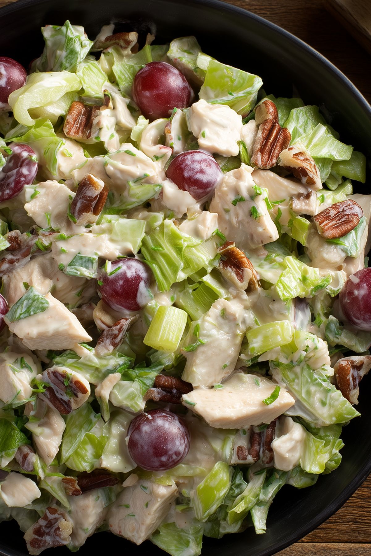 Close-up of creamy chicken salad with chopped chicken, red grapes, pecans, celery, and lettuce.
