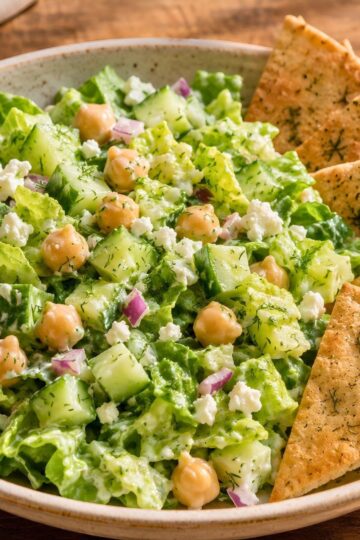 Creamy cucumber dill chickpea salad with chopped romaine, cucumber, chickpeas, red onion, feta, fresh dill, and creamy dressing, served in a bowl with toasted pita chips.