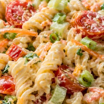 Creamy ranch vegetable pasta salad with rotini pasta, cherry tomatoes, broccoli, carrots, cucumber, green onions, and creamy ranch dressing in a close-up bowl.