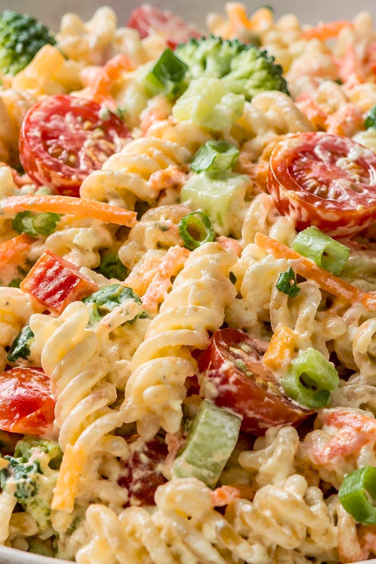 Creamy ranch vegetable pasta salad with rotini pasta, cherry tomatoes, broccoli, carrots, cucumber, green onions, and creamy ranch dressing in a close-up bowl.