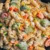Close-up of creamy ranch pasta salad with rotini, broccoli, cucumbers, tomatoes, bell peppers, cheddar cheese, and ranch dressing.