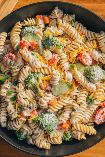 Close-up of creamy ranch pasta salad with rotini, broccoli, cucumbers, tomatoes, bell peppers, cheddar cheese, and ranch dressing.