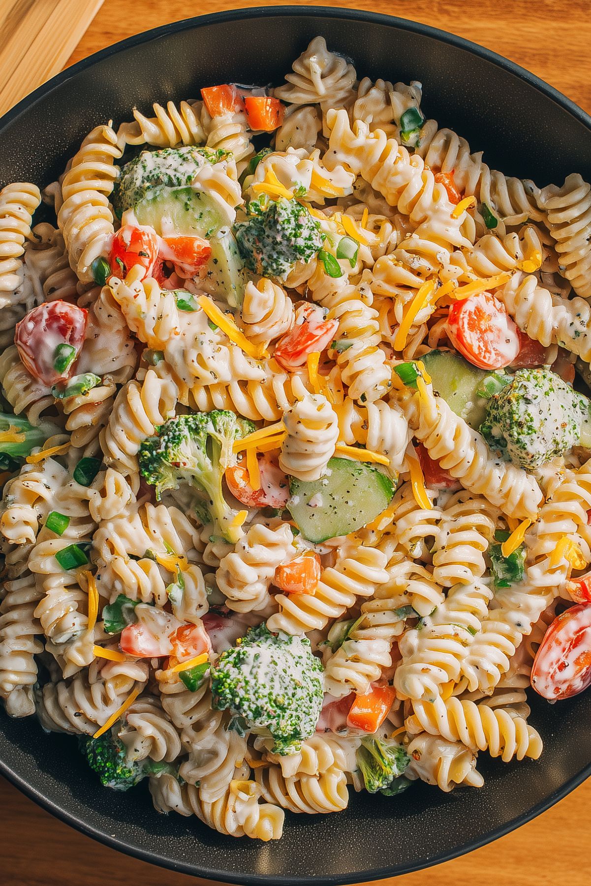 Close-up of creamy ranch pasta salad with rotini, broccoli, cucumbers, tomatoes, bell peppers, cheddar cheese, and ranch dressing.