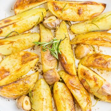 Golden grilled fingerling potatoes with roasted garlic cloves, rosemary, and southwest seasoning on a white plate.