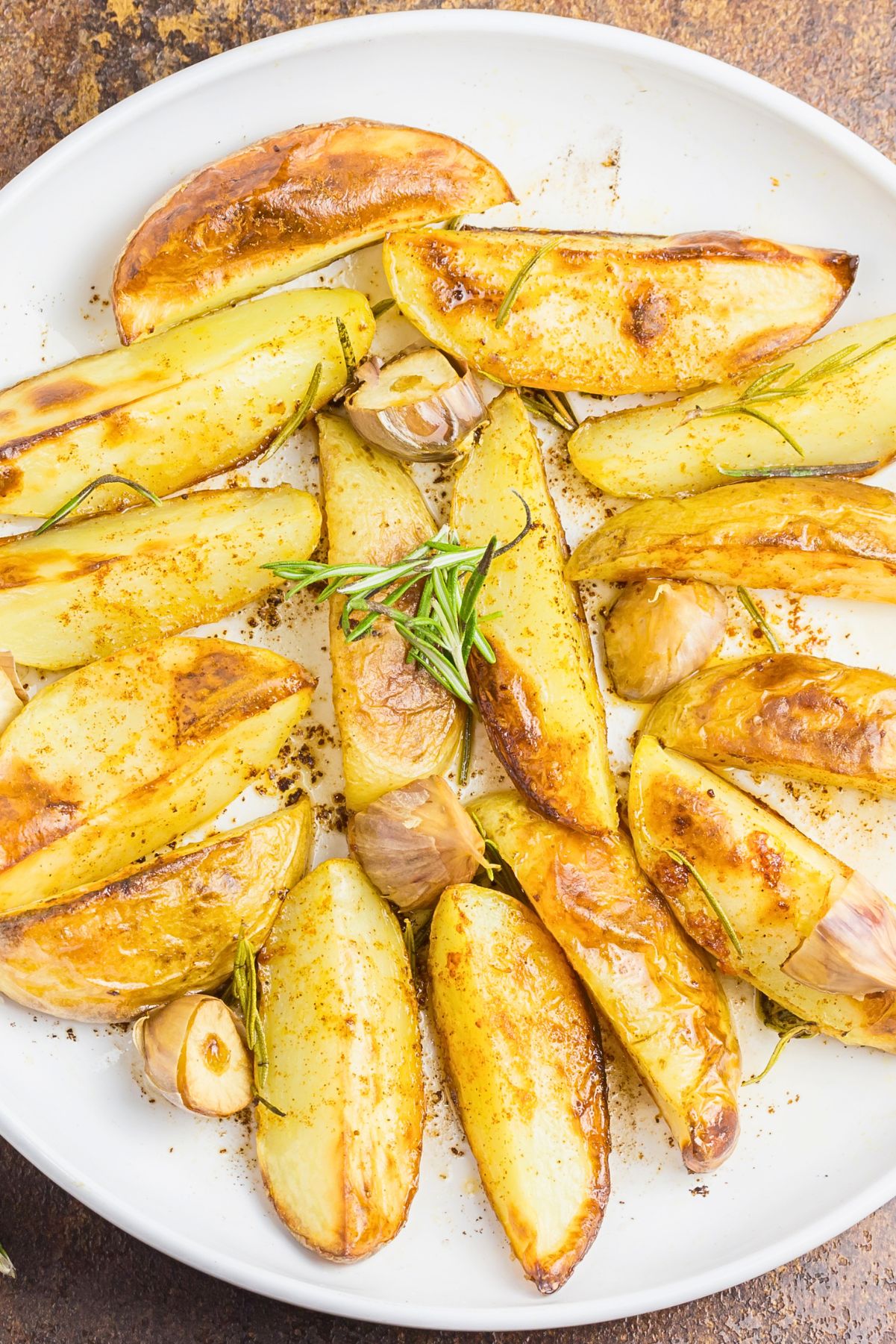 Golden grilled fingerling potatoes with roasted garlic cloves, rosemary, and southwest seasoning on a white plate.