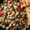 Close-up of Greek chickpea salad with cucumbers, tomatoes, red onion, olives, feta, and crispy garlic pita chips.