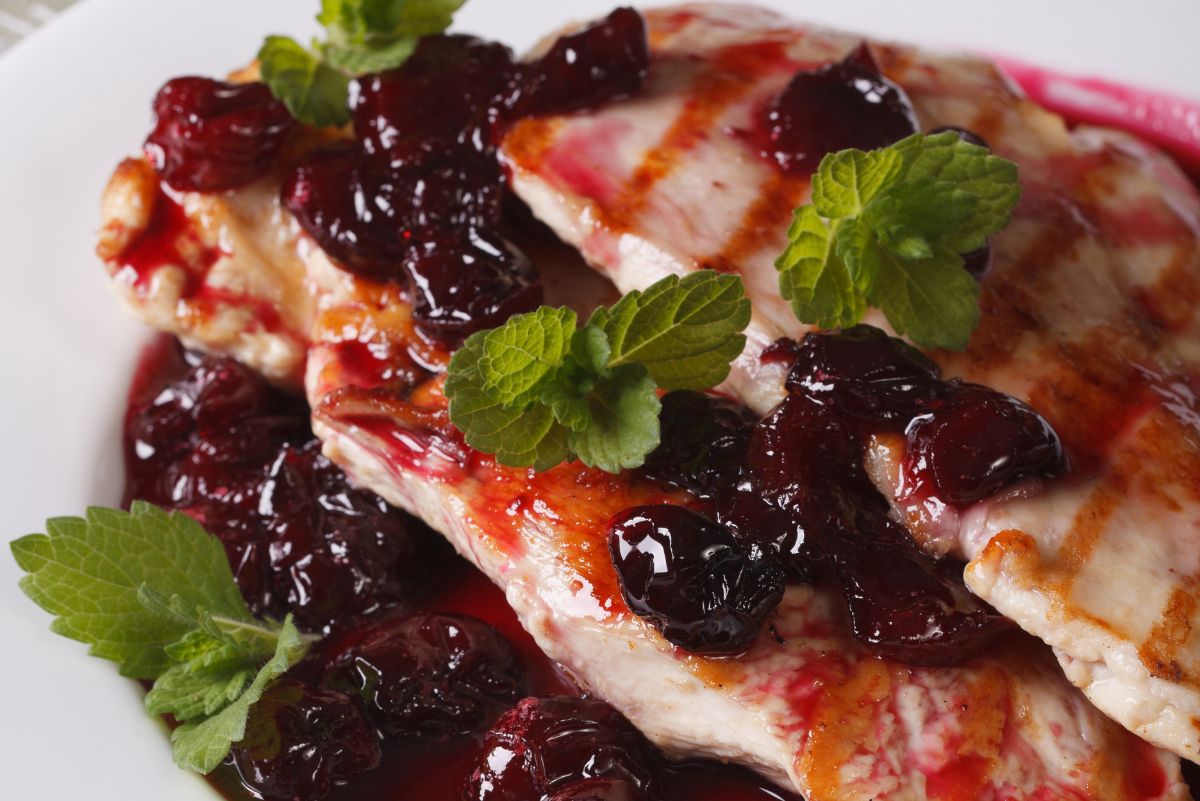 Grilled chicken with smoky cherry sauce, whole cherries, grill marks, and fresh mint on a white plate.
