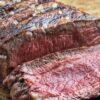 Sliced grilled sirloin steak on a wooden cutting board, showing a juicy pink center, seared crust, coarse salt, and herb seasoning.