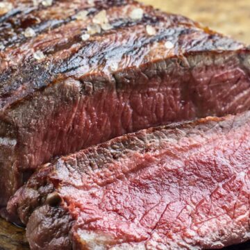 Sliced grilled sirloin steak on a wooden cutting board, showing a juicy pink center, seared crust, coarse salt, and herb seasoning.