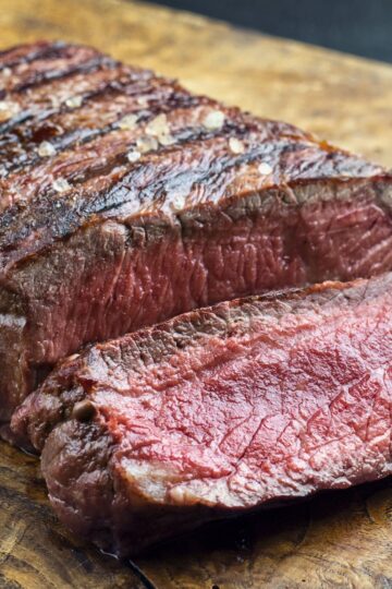 Sliced grilled sirloin steak on a wooden cutting board, showing a juicy pink center, seared crust, coarse salt, and herb seasoning.