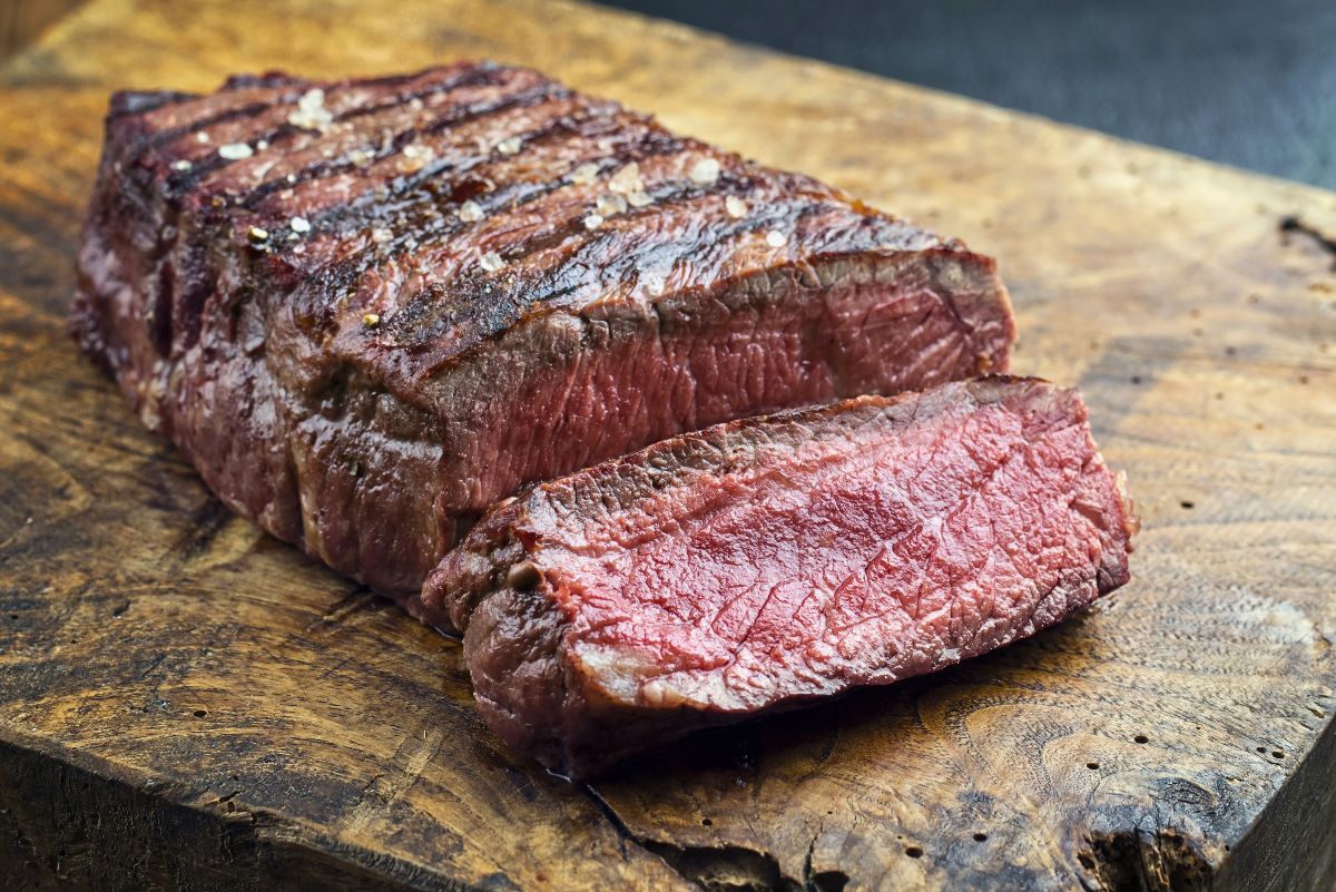 Grilled herb sirloin steak sliced on a rustic wooden cutting board, with a seared crust, coarse salt, and juicy pink center.