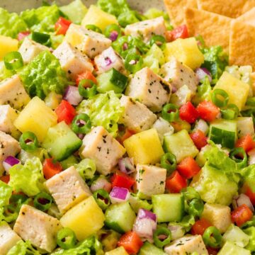 Hawaiian chicken chopped salad with romaine lettuce, diced chicken, pineapple, cucumber, red bell pepper, red onion, green onion, and crispy wonton chips in a shallow bowl.