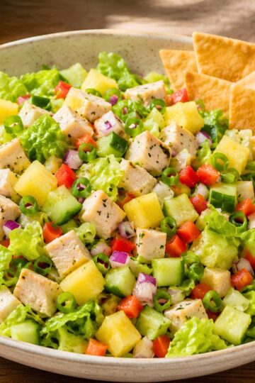 Hawaiian chicken chopped salad with romaine lettuce, diced chicken, pineapple, cucumber, red bell pepper, red onion, green onion, and crispy wonton chips in a shallow bowl.