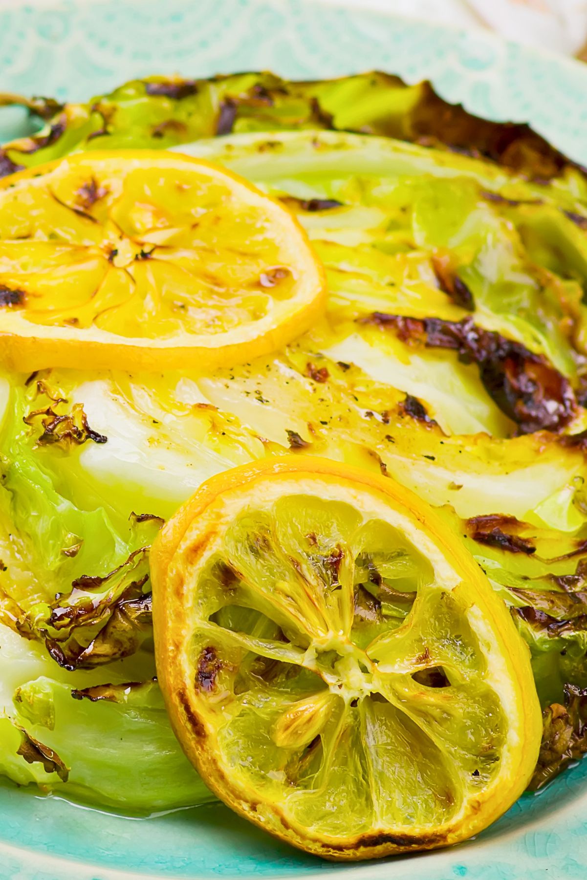 Grilled cabbage steaks with charred edges, black pepper, and roasted lemon slices on a turquoise plate. A bright summer cookout side dish with fresh lemon and lightly browned cabbage.