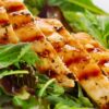 Sliced grilled chicken with visible grill marks and herb seasoning served over fresh mixed greens for a simple grilled chicken salad.