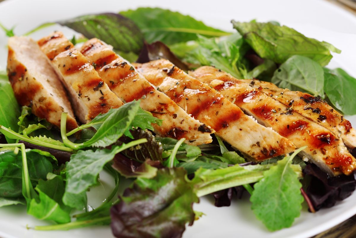 Sliced Herbes de Provence grilled chicken with charred grill marks and herb seasoning served over fresh mixed greens on a white plate.