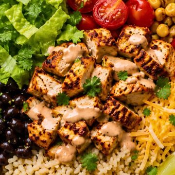 High protein chicken burrito bowl with grilled chicken, rice, black beans, corn, romaine lettuce, cherry tomatoes, shredded cheese, cilantro, lime, and creamy sauce.