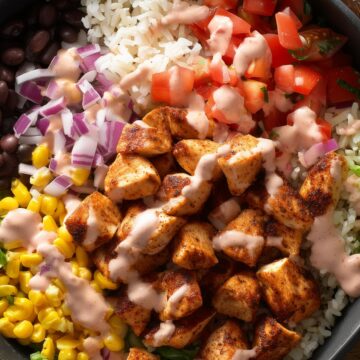Close-up of a high-protein chicken burrito bowl with grilled chicken, rice, black beans, corn, diced tomatoes, red onion, and creamy dressing.