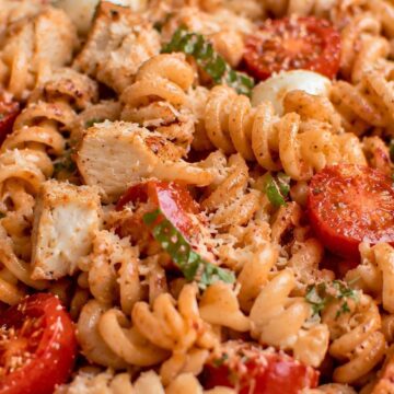 High protein chicken Parmesan pasta salad with rotini, diced chicken breast, cherry tomatoes, mozzarella, basil, marinara sauce, and grated Parmesan in a white bowl.