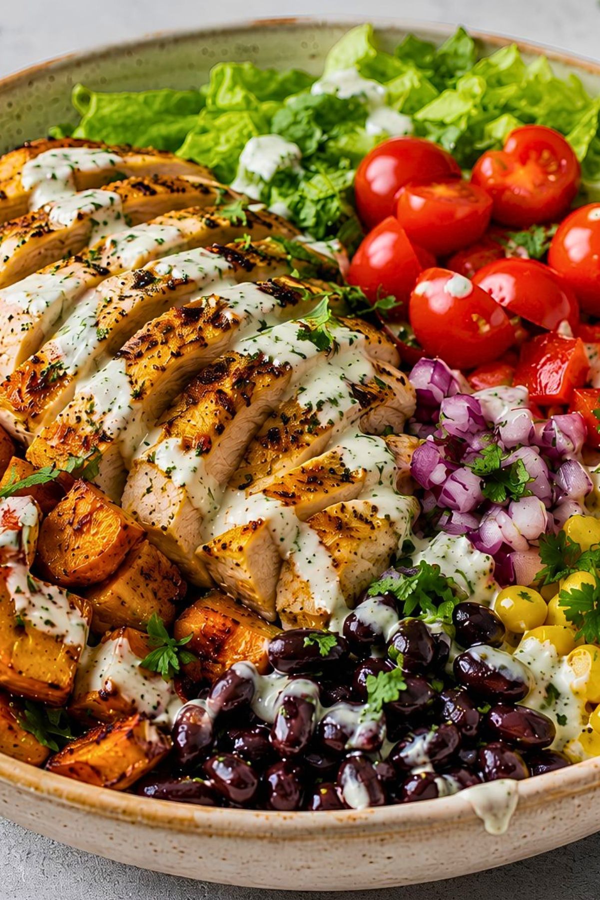 High protein chicken sweet potato bowl with sliced grilled chicken, roasted sweet potatoes, black beans, corn, tomatoes, red onion, romaine lettuce, cilantro, and creamy herb dressing in a large ceramic bowl.