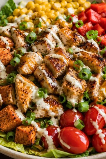 Hot honey chicken sweet potato bowl with grilled chicken, roasted sweet potatoes, corn, red peppers, cherry tomatoes, green onions, romaine, and creamy sauce.