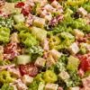 Italian grinder chopped salad with romaine lettuce, deli meat, provolone cubes, cucumber, cherry tomatoes, banana peppers, black olives, and creamy dressing in a white bowl.