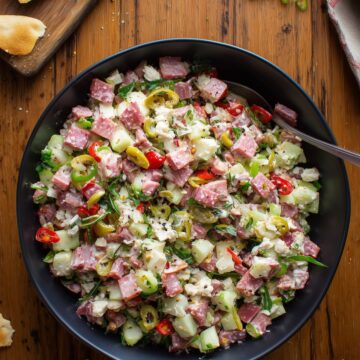 Italian grinder chopped salad with turkey, ham, salami, provolone, chopped vegetables, banana peppers, and garlic pita chips on a rustic wooden table.
