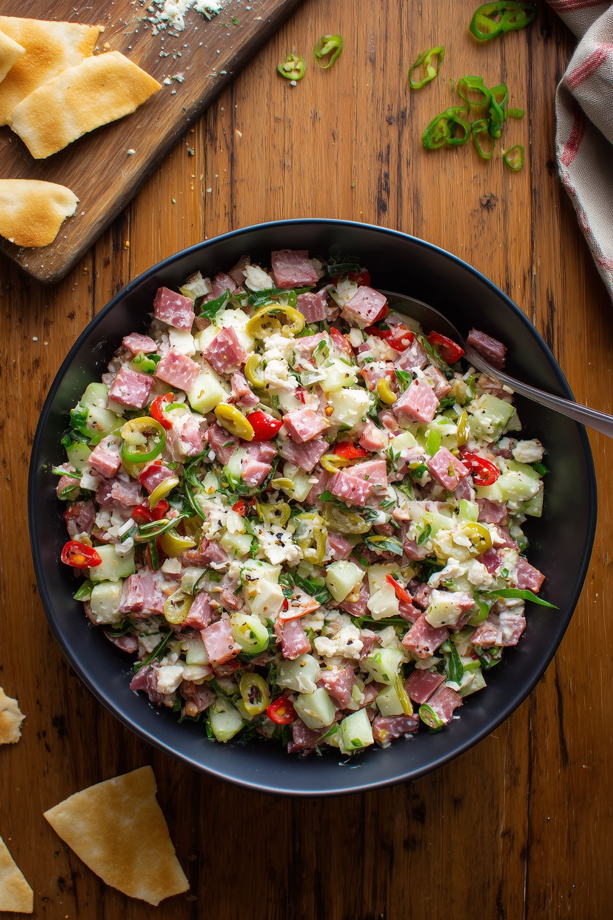 Italian grinder chopped salad with turkey, ham, salami, provolone, chopped vegetables, banana peppers, and garlic pita chips on a rustic wooden table.