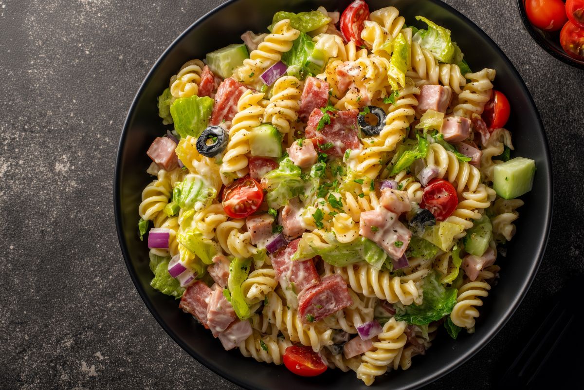 Overhead view of Italian grinder pasta salad with rotini, deli meats, lettuce, cherry tomatoes, cucumbers, red onion, black olives, and creamy Italian dressing.