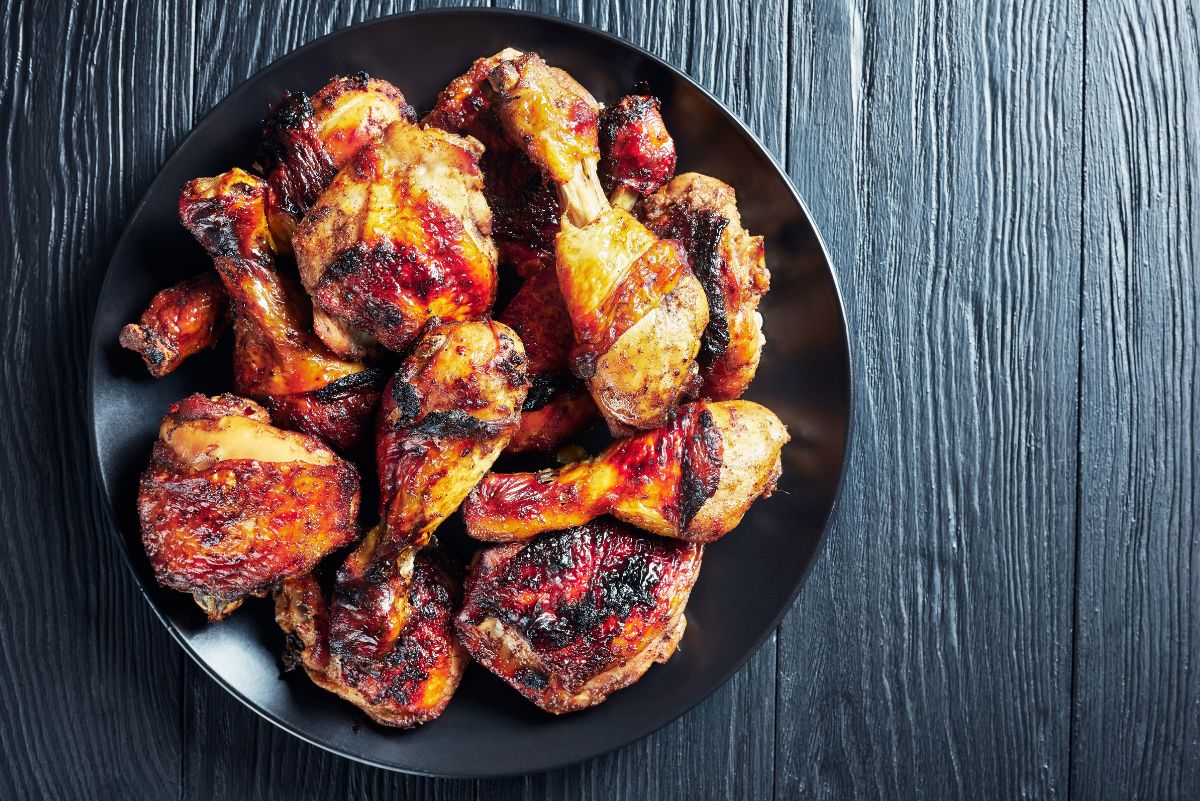 Jamaican jerk chicken drumsticks and thighs with charred golden skin piled on a black plate, served over a dark wood background.