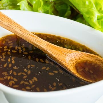 Japanese sesame soy salad dressing in a white bowl with sesame seeds, a wooden spoon, and fresh green lettuce in the background.