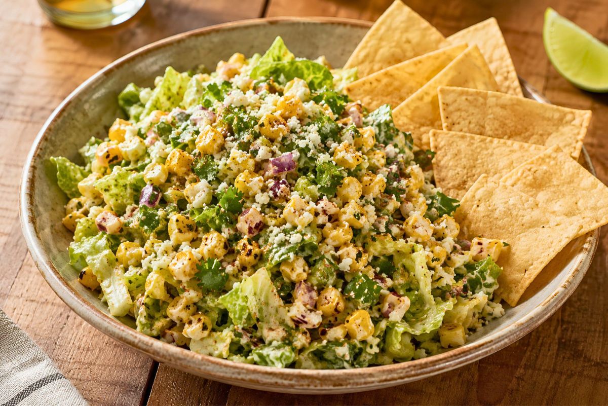 Mexican street corn chopped salad with romaine lettuce, roasted corn, red onion, cilantro, cotija cheese, and creamy chili-lime dressing served with tortilla chips and a lime wedge.