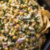 Mexican street corn chopped salad with corn, cotija cheese, red onion, cilantro, chopped greens, and tortilla chips in a black bowl.
