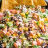 Close-up of Southwest chopped salad with black beans, corn, tomatoes, bell peppers, red onion, creamy dressing, and tortilla chips.