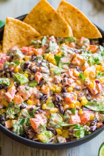 Close-up of Southwest chopped salad with black beans, corn, tomatoes, bell peppers, red onion, creamy dressing, and tortilla chips.